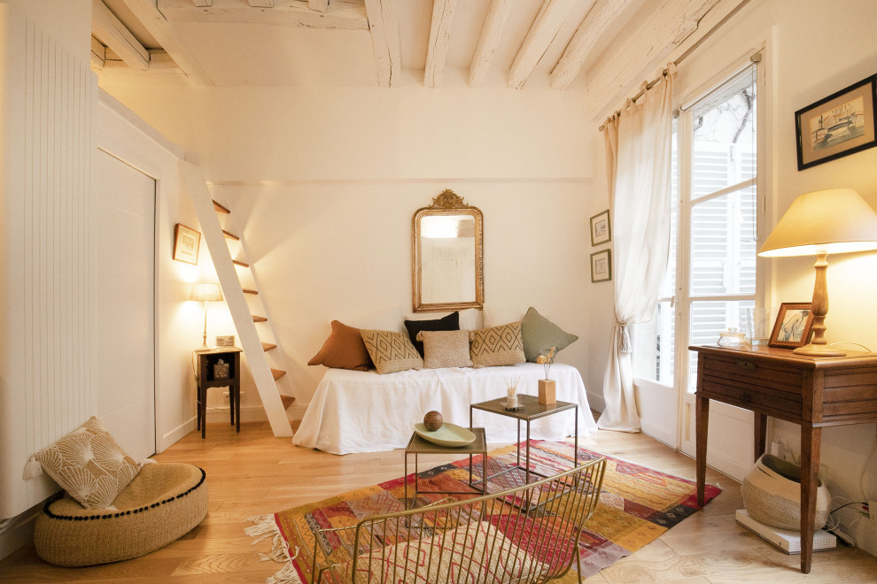 Modelo de sala de estar abierta clásica pequeña sin chimenea y televisor con paredes blancas, suelo de madera clara, suelo beige, vigas vistas y ladrillo