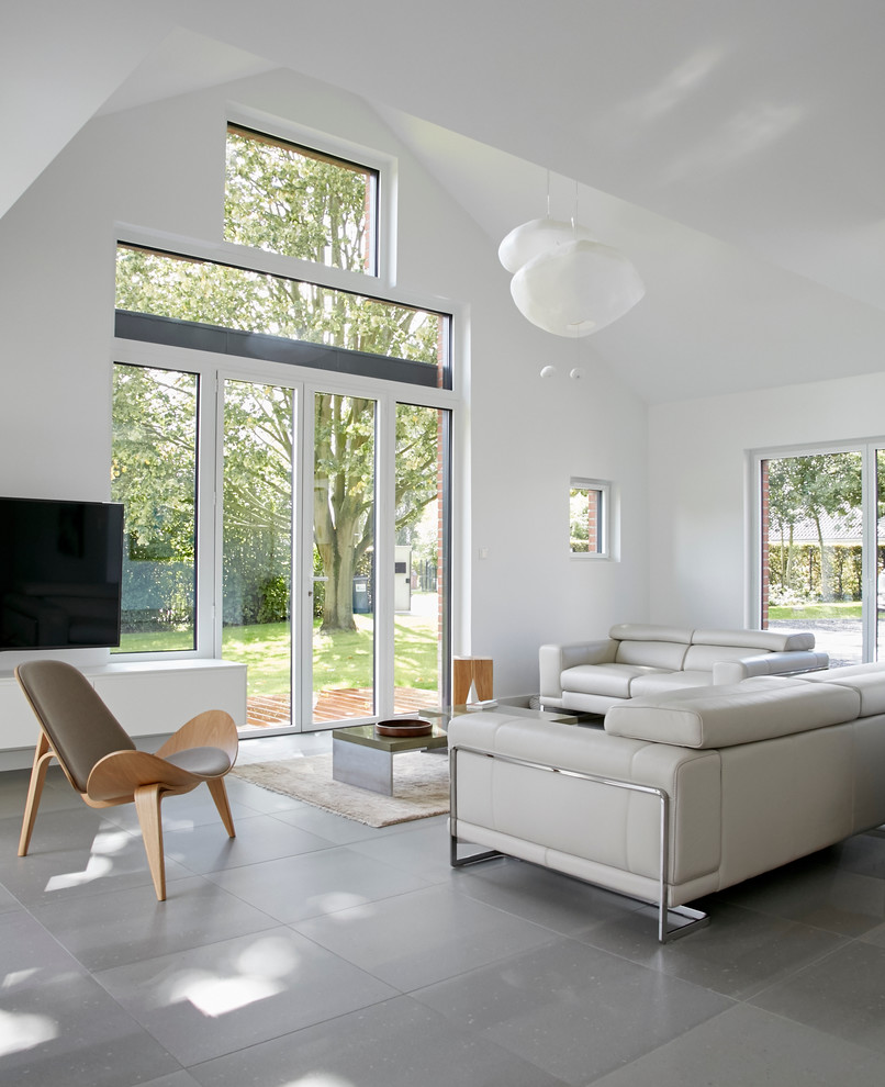 Пример оригинального дизайна: открытая гостиная комната среднего размера в скандинавском стиле с белыми стенами, полом из керамической плитки, телевизором на стене и серым полом без камина