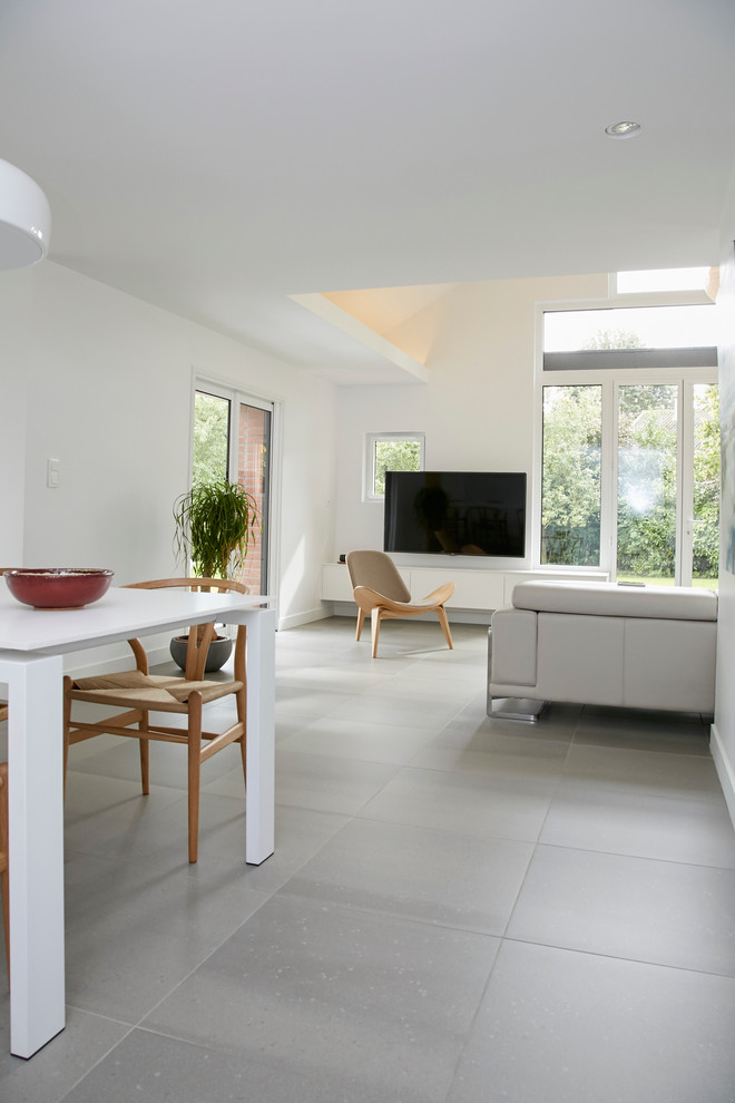 Diseño de sala de estar abierta nórdica de tamaño medio con paredes blancas, suelo de baldosas de cerámica, televisor colgado en la pared y suelo gris