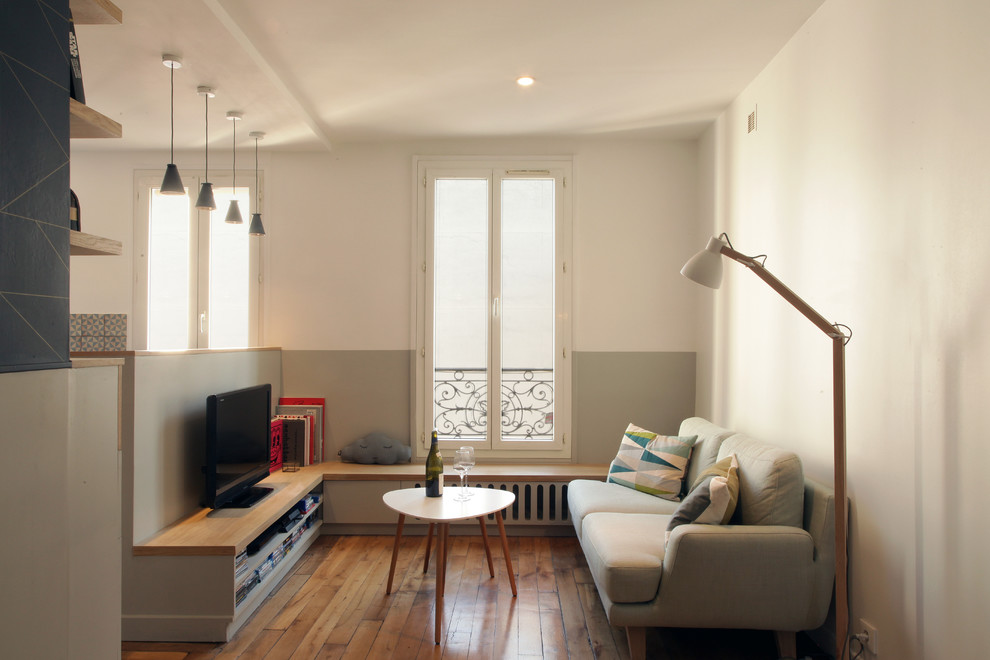 Modelo de sala de estar abierta escandinava pequeña sin chimenea con televisor colgado en la pared, paredes multicolor y suelo de madera en tonos medios