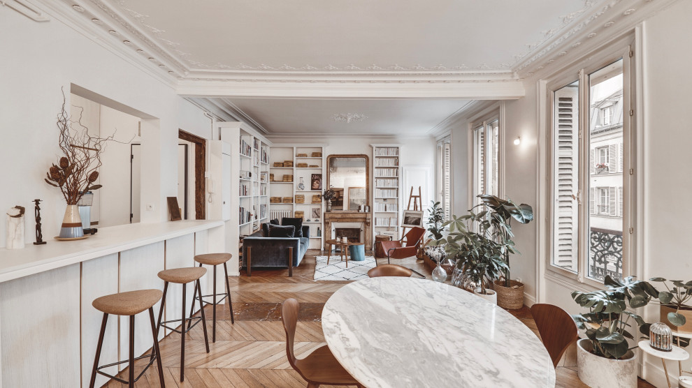 パリにある高級な広い北欧スタイルのおしゃれなオープンリビング (ライブラリー、白い壁、無垢フローリング、標準型暖炉、石材の暖炉まわり、テレビなし、茶色い床、羽目板の壁) の写真