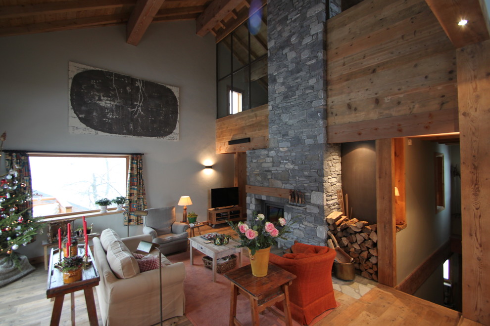 Réalisation d'une salle de séjour chalet de taille moyenne et ouverte avec un mur gris, un sol en bois brun, une cheminée standard, un manteau de cheminée en pierre et un téléviseur indépendant.