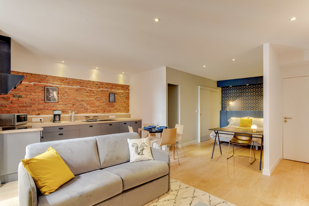 Imagen de sala de estar abierta contemporánea pequeña con parades naranjas, suelo de madera clara y televisor independiente