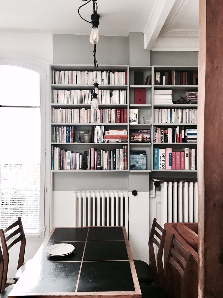 Ejemplo de sala de estar con biblioteca abierta actual pequeña con paredes grises, suelo de madera clara, chimenea de esquina, marco de chimenea de piedra, televisor independiente y suelo marrón