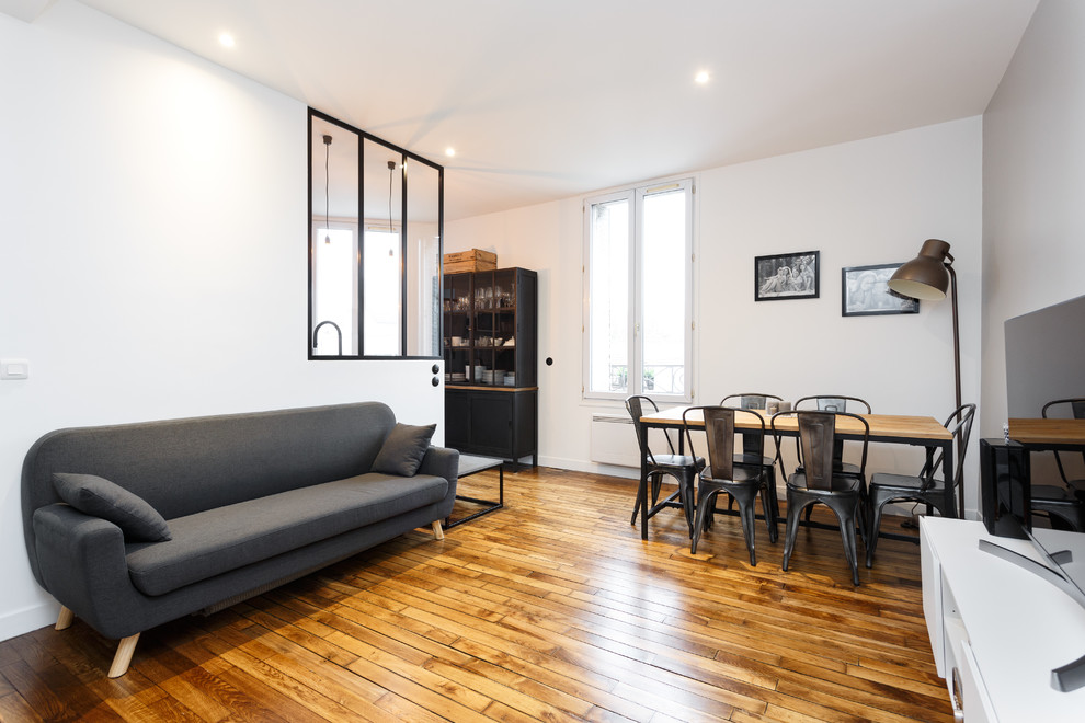 Modelo de sala de estar abierta moderna pequeña sin chimenea con paredes blancas, suelo de madera en tonos medios, televisor independiente y suelo marrón