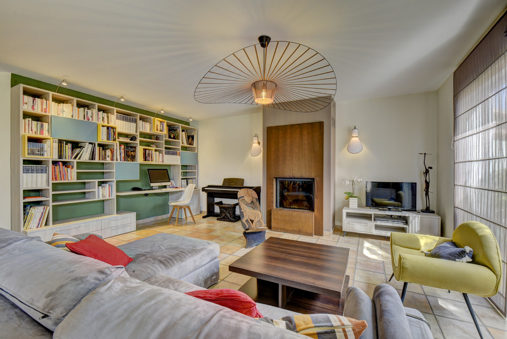 This is an example of a large contemporary open plan games room in Other with a reading nook, green walls, terracotta flooring, a standard fireplace, a metal fireplace surround, a freestanding tv and brown floors.