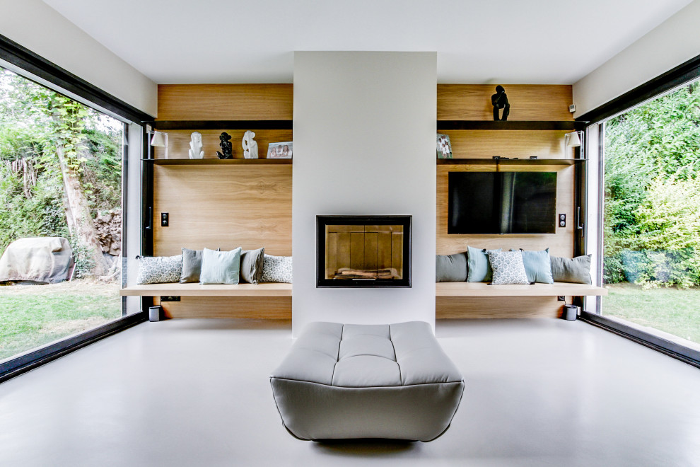 Ejemplo de sala de estar abierta contemporánea extra grande con paredes beige, suelo de cemento, chimenea de doble cara, marco de chimenea de yeso, televisor colgado en la pared, suelo gris y madera