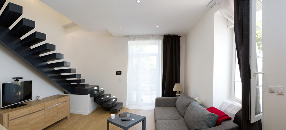 Imagen de sala de estar abierta actual sin chimenea con paredes blancas, suelo de madera en tonos medios y televisor independiente