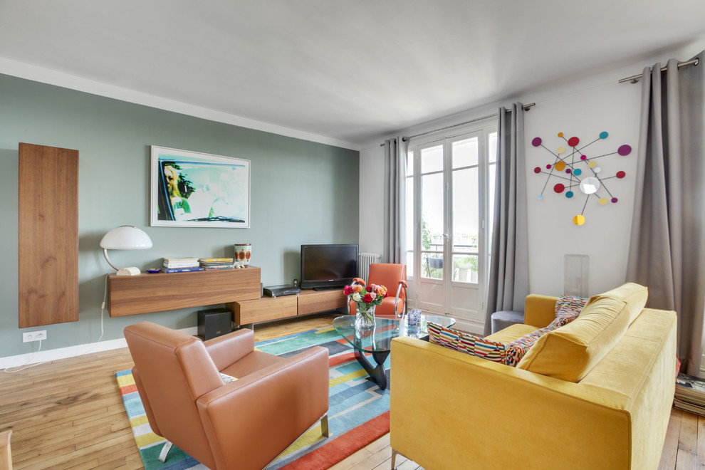 Cette image montre une salle de séjour design de taille moyenne et ouverte avec parquet clair, un téléviseur indépendant, un sol marron, un mur vert et aucune cheminée.