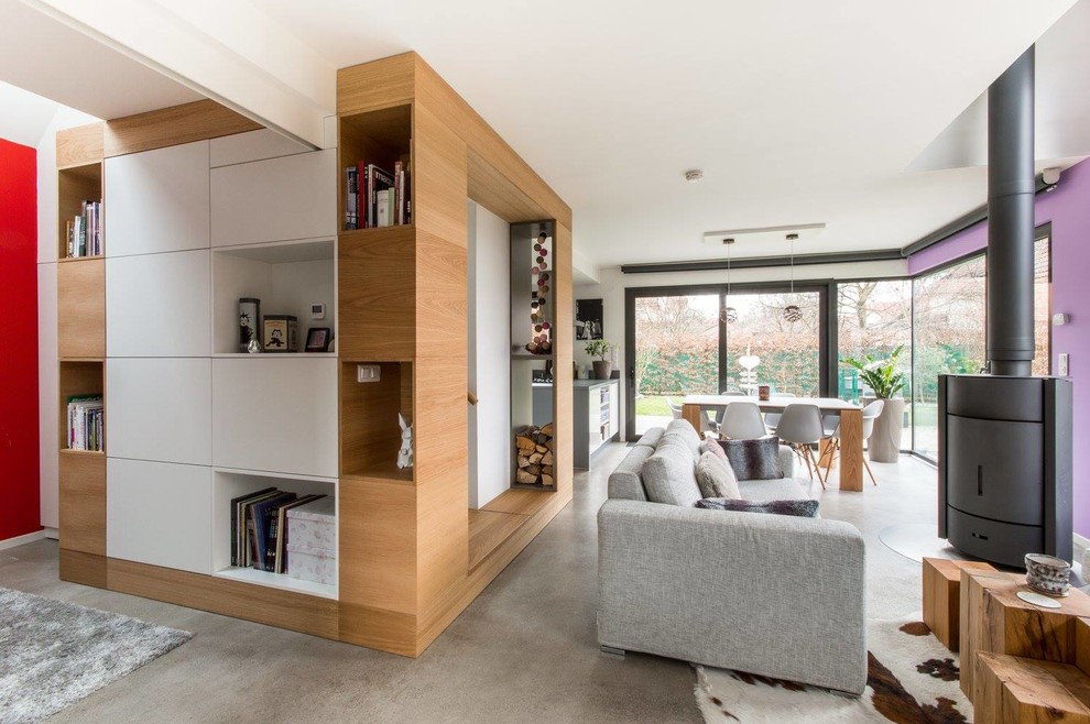 Diseño de sala de estar con biblioteca abierta nórdica grande con paredes blancas, suelo de cemento, estufa de leña y suelo gris