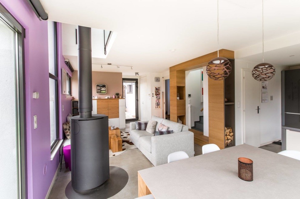 This is an example of a large open plan games room in Strasbourg with white walls, concrete flooring, a wood burning stove, a concealed tv and grey floors.