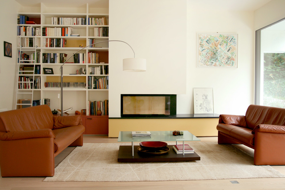 Imagen de sala de estar con biblioteca abierta actual grande sin televisor con paredes blancas y suelo de madera clara