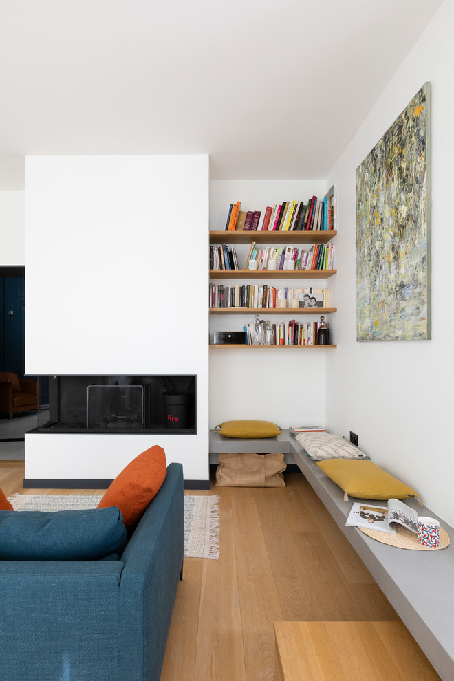Diseño de sala de estar con biblioteca abierta actual de tamaño medio sin televisor con paredes blancas, suelo de madera clara, estufa de leña y suelo beige