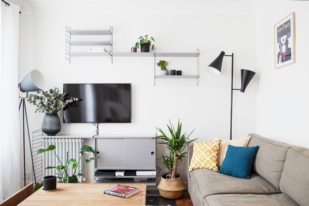 Modelo de sala de estar con biblioteca abierta nórdica pequeña con paredes beige, suelo de madera clara y televisor colgado en la pared
