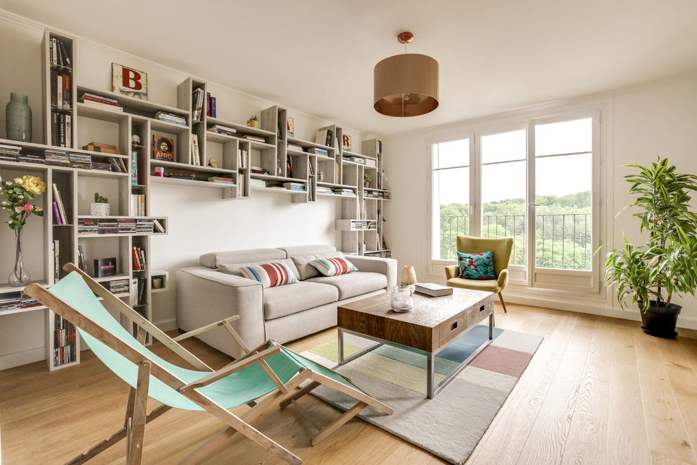 Cette image montre une salle de séjour design ouverte avec une bibliothèque ou un coin lecture, un mur blanc, parquet clair et un sol beige.