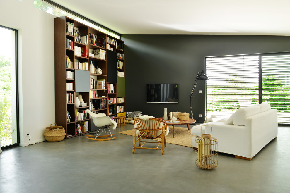 Cette photo montre une salle de séjour tendance ouverte avec une bibliothèque ou un coin lecture, un mur gris, sol en béton ciré et un téléviseur fixé au mur.