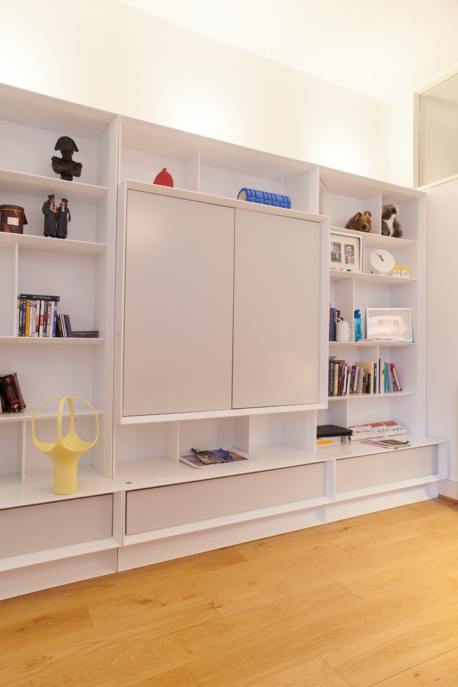 Diseño de sala de estar con biblioteca cerrada contemporánea con paredes blancas, suelo de madera en tonos medios, televisor retractable y suelo marrón