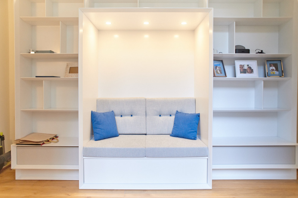 Идея дизайна: изолированная гостиная комната в современном стиле с с книжными шкафами и полками, белыми стенами, паркетным полом среднего тона, скрытым телевизором и коричневым полом