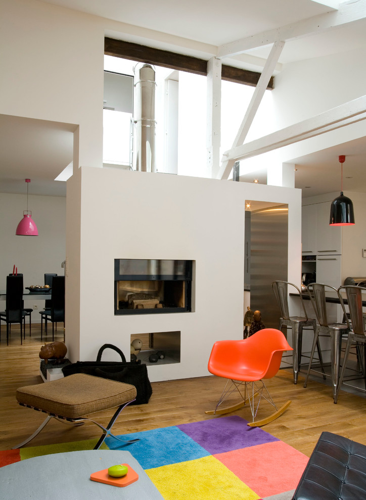 Diseño de salón abierto industrial de tamaño medio sin televisor con paredes blancas, suelo de madera en tonos medios y chimenea de doble cara