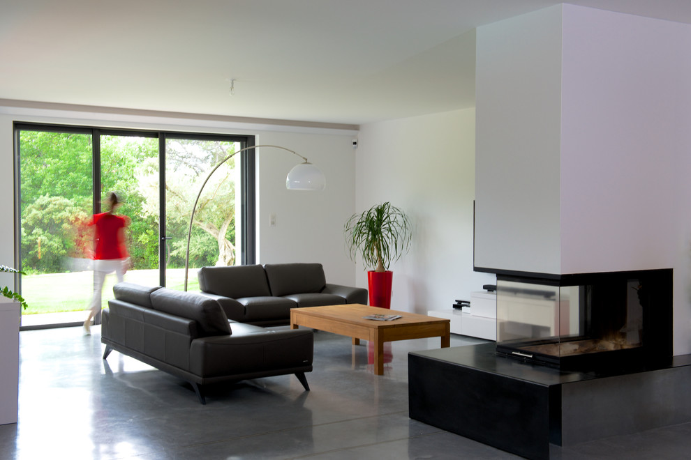 Imagen de sala de estar con biblioteca abierta contemporánea con paredes blancas, suelo de cemento, todas las chimeneas, marco de chimenea de metal, televisor independiente y suelo gris