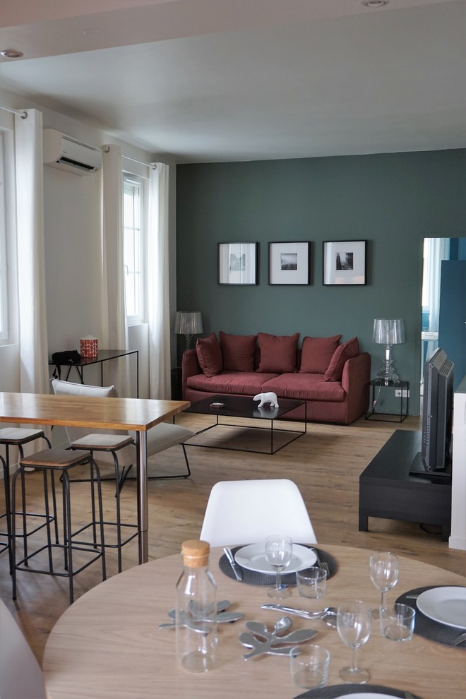 Modelo de sala de estar abierta tradicional renovada de tamaño medio con paredes verdes, suelo de madera clara y televisor independiente