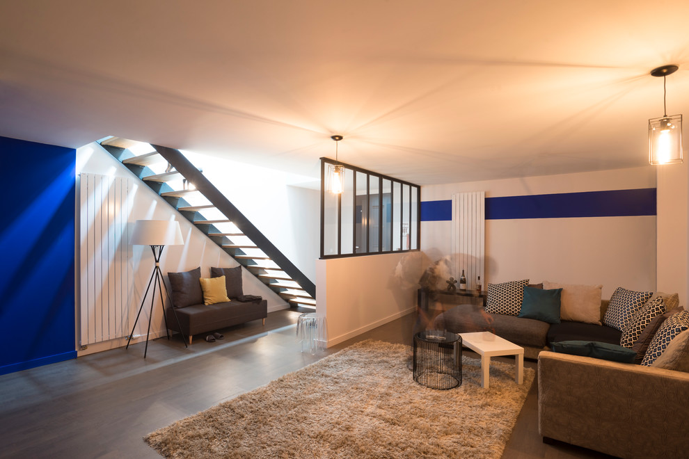 Cette image montre une grande salle de séjour design ouverte avec un mur bleu et un sol en bois brun.