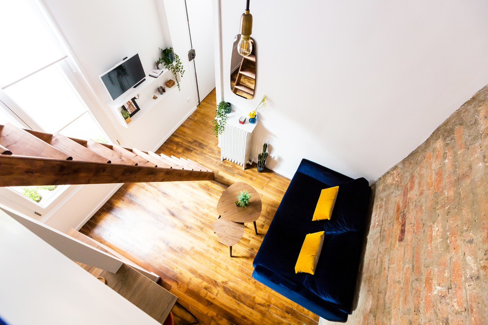 Exemple d'une petite salle de séjour mansardée ou avec mezzanine industrielle avec un bar de salon, un mur blanc, un sol en bois brun, un téléviseur fixé au mur et un sol marron.