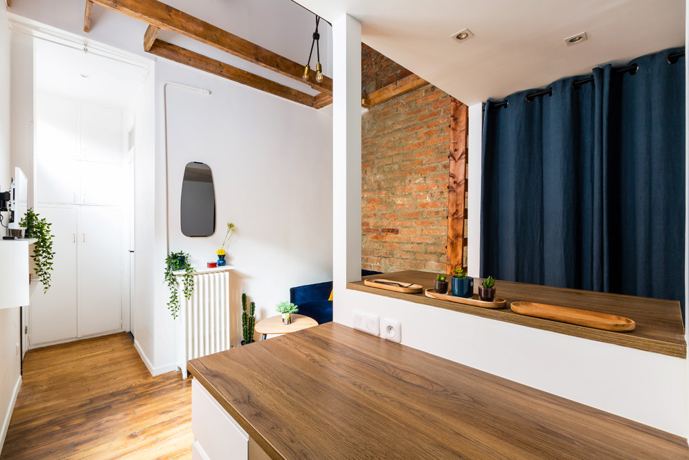 Exemple d'une petite salle de séjour mansardée ou avec mezzanine industrielle avec un bar de salon, un mur blanc, un sol en bois brun, aucune cheminée, un téléviseur fixé au mur et un sol marron.