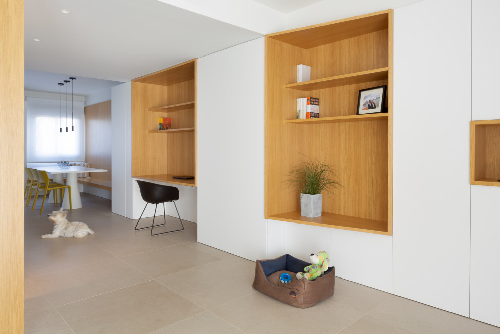 Immagine di un soggiorno nordico di medie dimensioni e aperto con libreria, pareti bianche, pavimento in gres porcellanato, porta TV ad angolo e pavimento beige