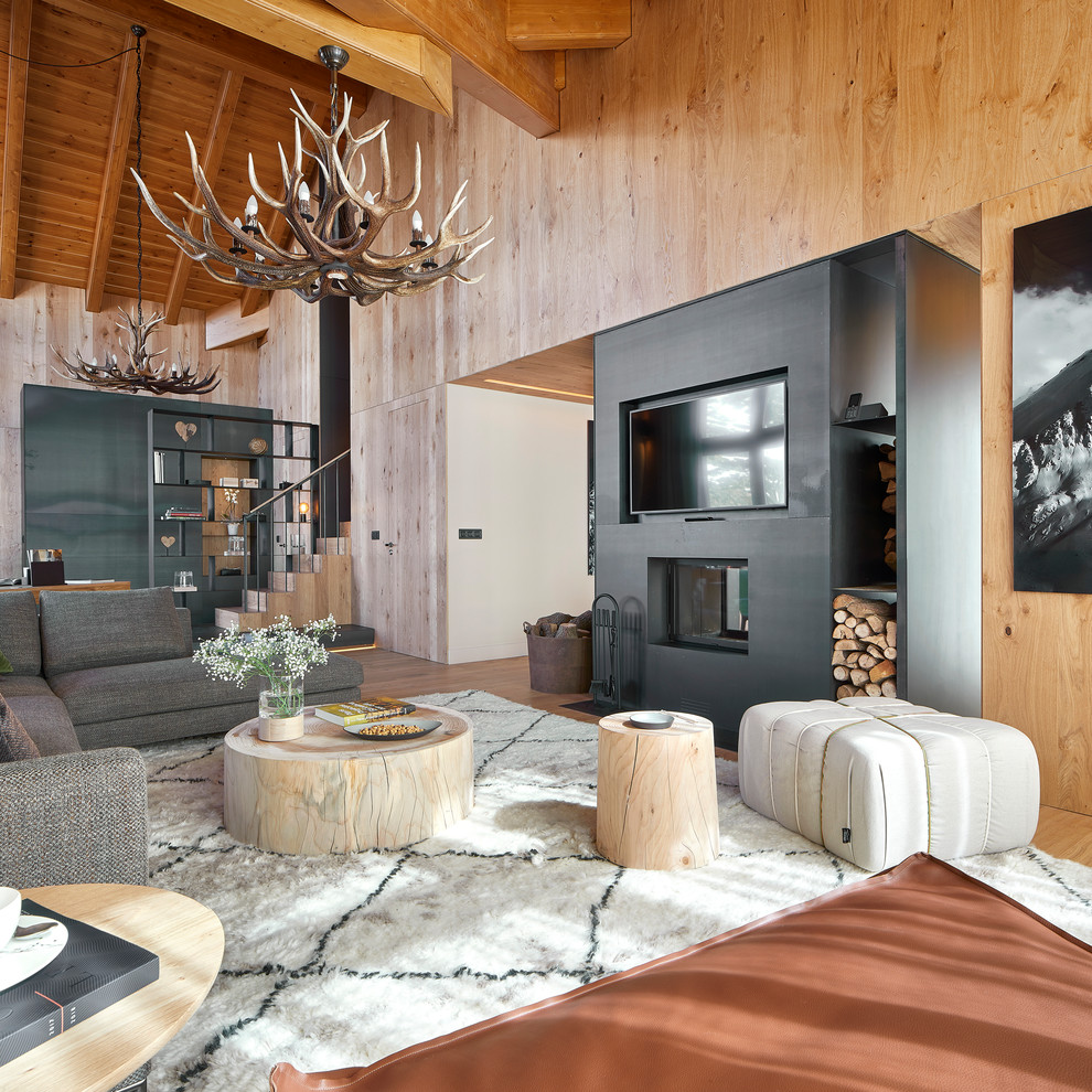 Ejemplo de salón abierto moderno grande con suelo de madera en tonos medios, chimenea de doble cara, marco de chimenea de metal y televisor colgado en la pared