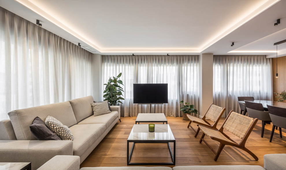 Modelo de salón abierto actual con paredes grises, suelo de madera en tonos medios, televisor independiente y suelo marrón