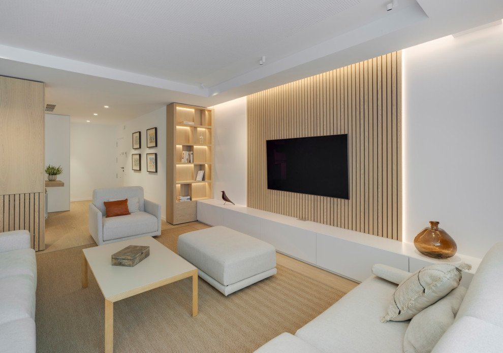 Modelo de biblioteca en casa contemporánea con paredes blancas, suelo de madera clara y televisor colgado en la pared