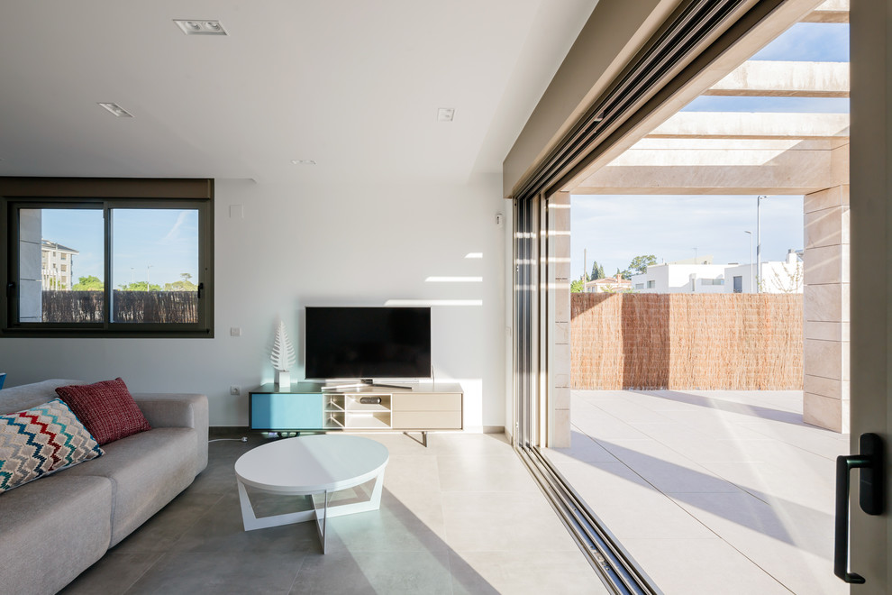 Идея дизайна: огромная открытая гостиная комната в стиле модернизм с белыми стенами, полом из керамогранита, отдельно стоящим телевизором и серым полом без камина