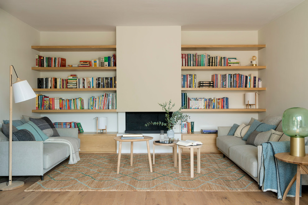 Diseño de biblioteca en casa nórdica de tamaño medio sin televisor con paredes beige, suelo de madera clara, estufa de leña y suelo marrón