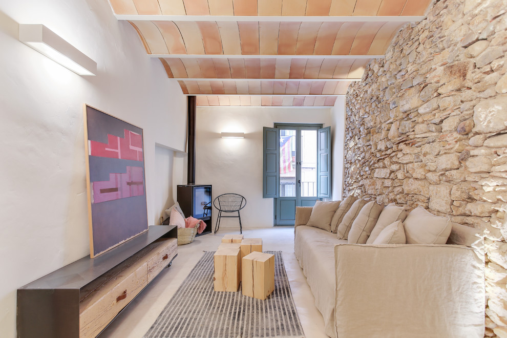 Mittelgroßes, Fernseherloses Mediterranes Wohnzimmer mit weißer Wandfarbe, Betonboden, Kaminofen, grauem Boden und Steinwänden in Sonstige
