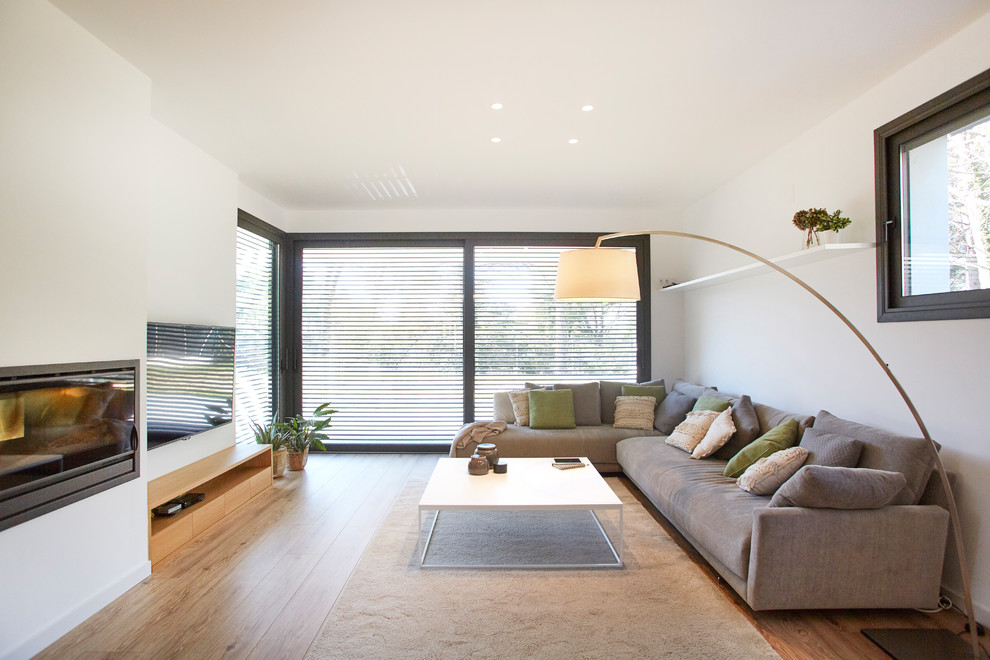 Photo of a modern formal enclosed living room in Barcelona with white walls, medium hardwood flooring, a ribbon fireplace, a wall mounted tv and beige floors.