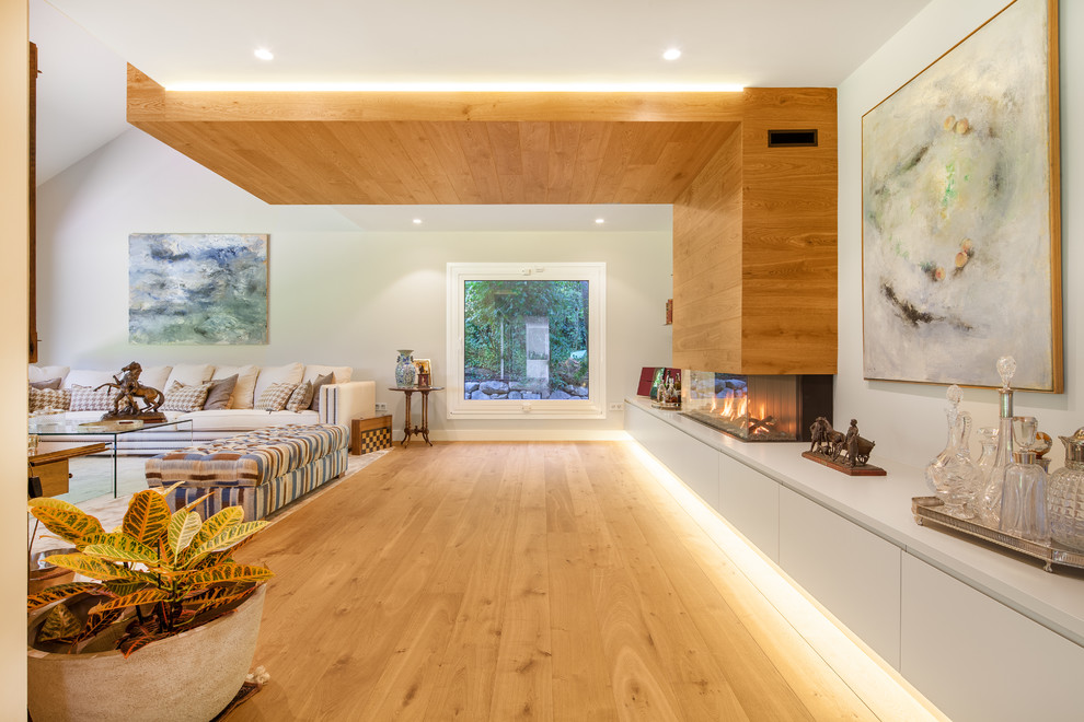 Diseño de salón para visitas abierto contemporáneo grande sin televisor con paredes blancas, chimenea lineal, marco de chimenea de madera y suelo de madera clara