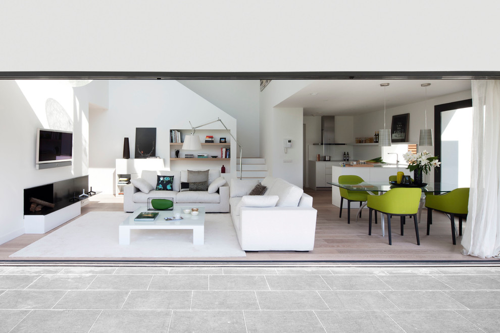 На фото: открытая гостиная комната среднего размера в современном стиле с белыми стенами и телевизором на стене с