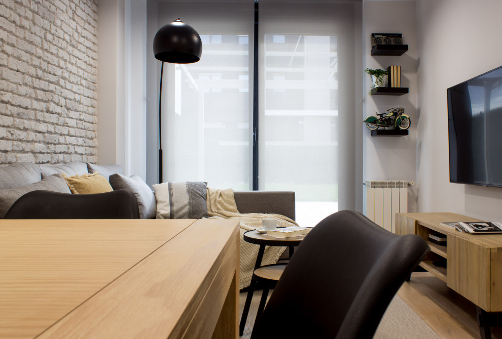 Diseño de salón cerrado escandinavo pequeño con paredes grises, suelo de madera clara, televisor colgado en la pared y ladrillo
