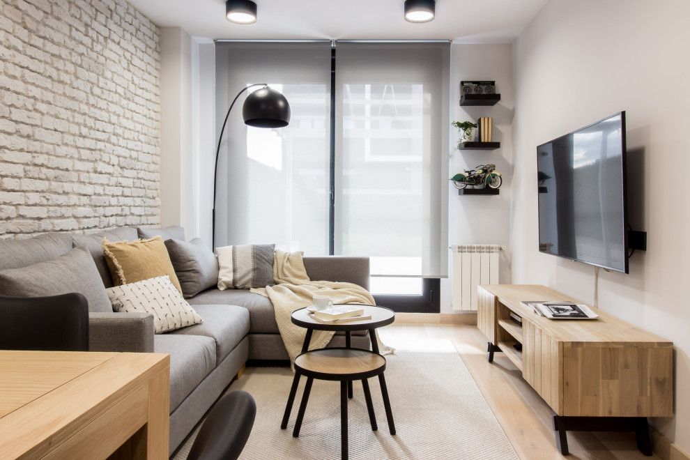Стильный дизайн: маленькая изолированная гостиная комната с серыми стенами, светлым паркетным полом, телевизором на стене и кирпичными стенами для на участке и в саду - последний тренд