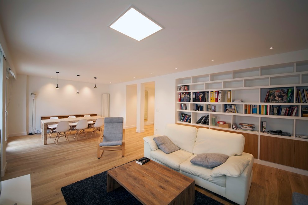 На фото: открытая гостиная комната среднего размера в скандинавском стиле с с книжными шкафами и полками, белыми стенами и паркетным полом среднего тона без камина