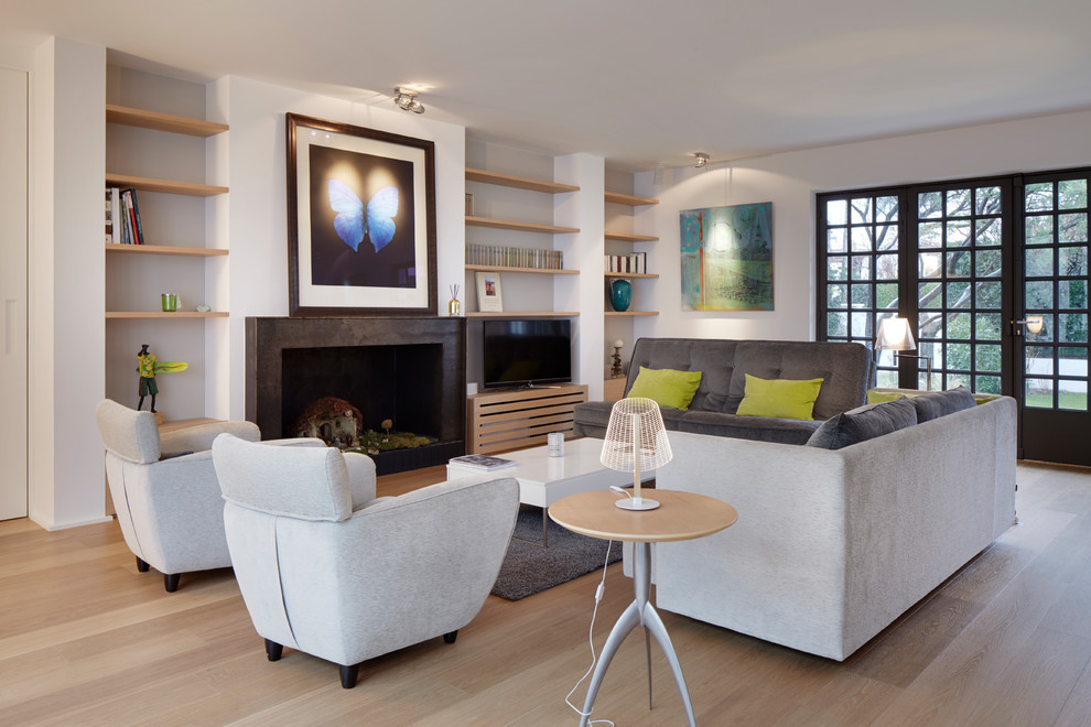 Diseño de salón para visitas abierto contemporáneo con paredes blancas, suelo de madera clara, todas las chimeneas, marco de chimenea de metal, televisor independiente y suelo beige