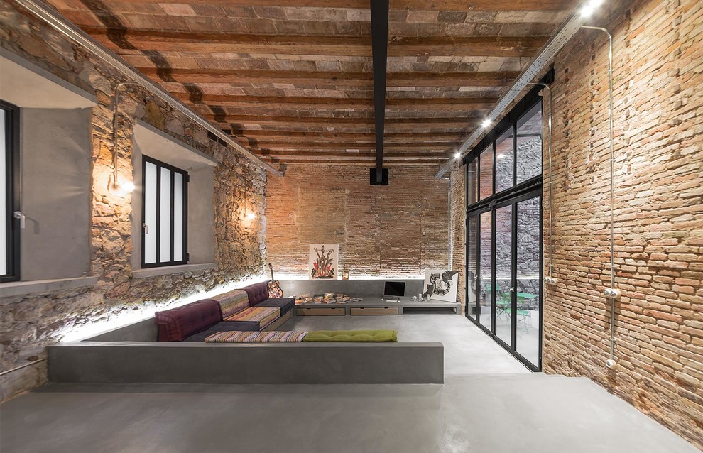 Offenes Industrial Wohnzimmer mit beiger Wandfarbe, Betonboden, grauem Boden und Steinwänden in Barcelona