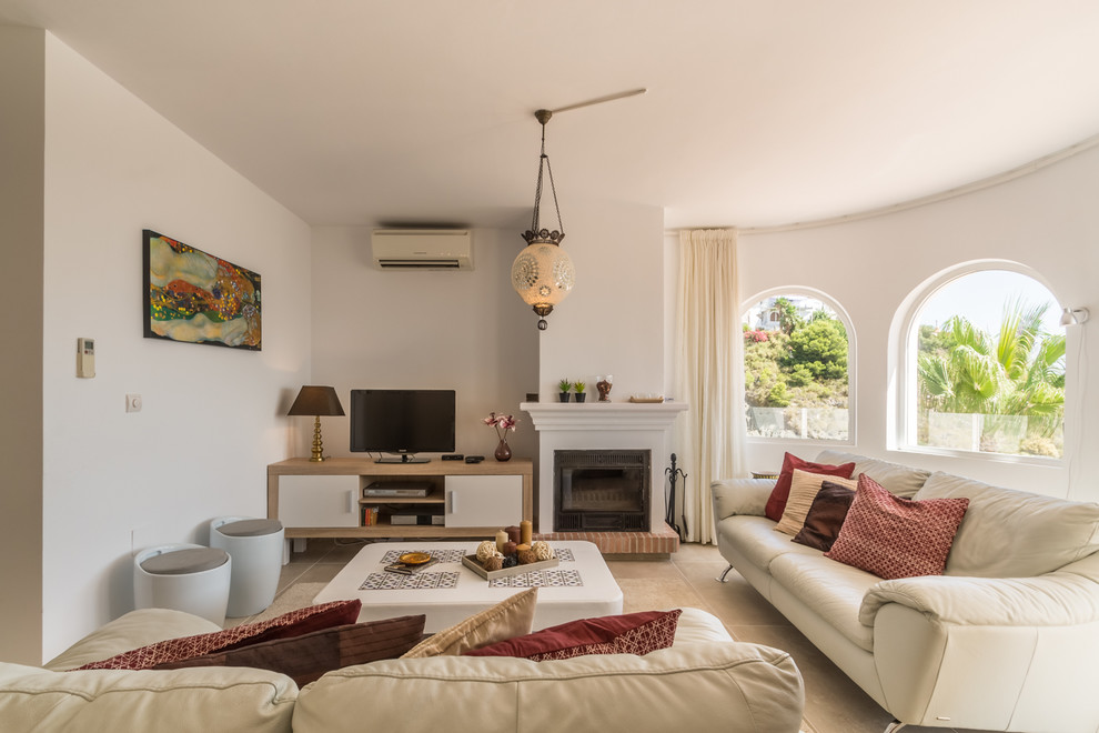 Ejemplo de salón para visitas cerrado mediterráneo con paredes blancas, todas las chimeneas, marco de chimenea de ladrillo, televisor independiente y suelo beige