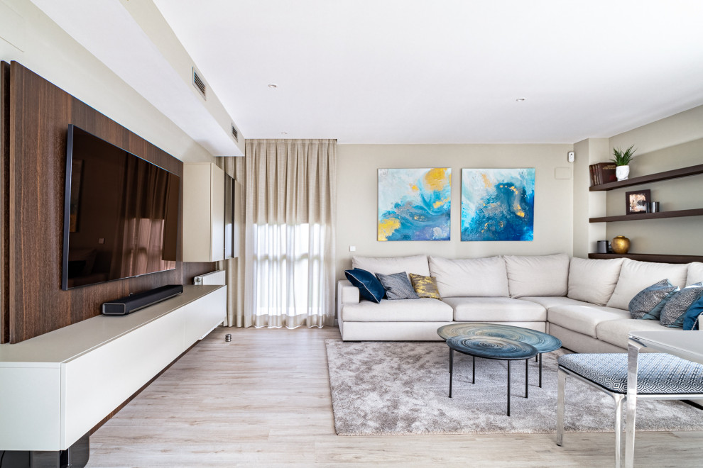 Ejemplo de salón abierto actual grande con paredes beige, suelo de madera clara, televisor colgado en la pared y suelo beige
