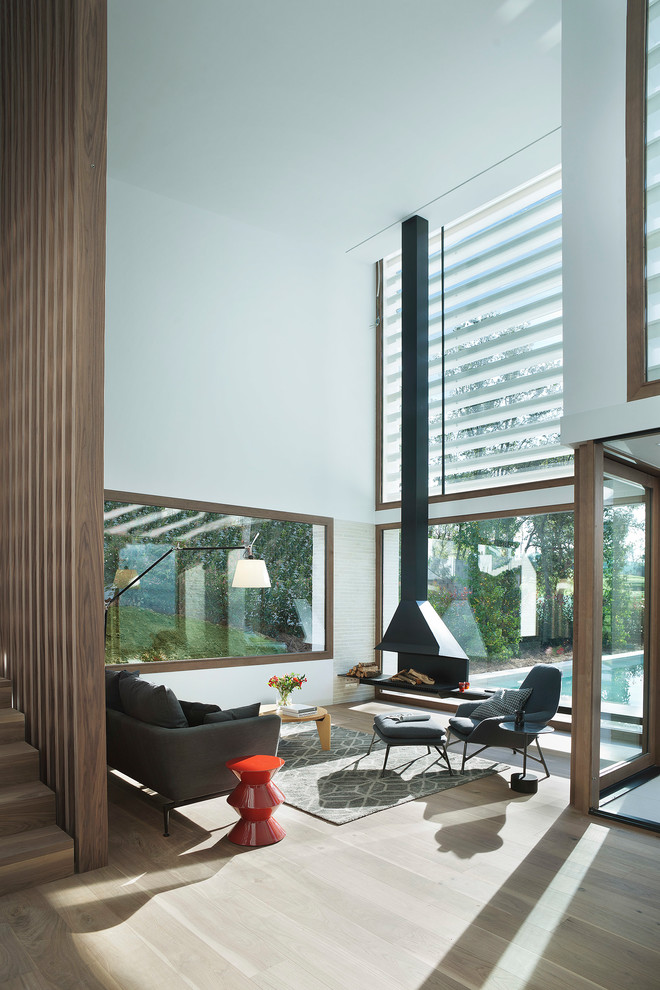 Cette photo montre un grand salon moderne fermé avec un mur blanc, un sol en bois brun, cheminée suspendue, aucun téléviseur et canapé noir.