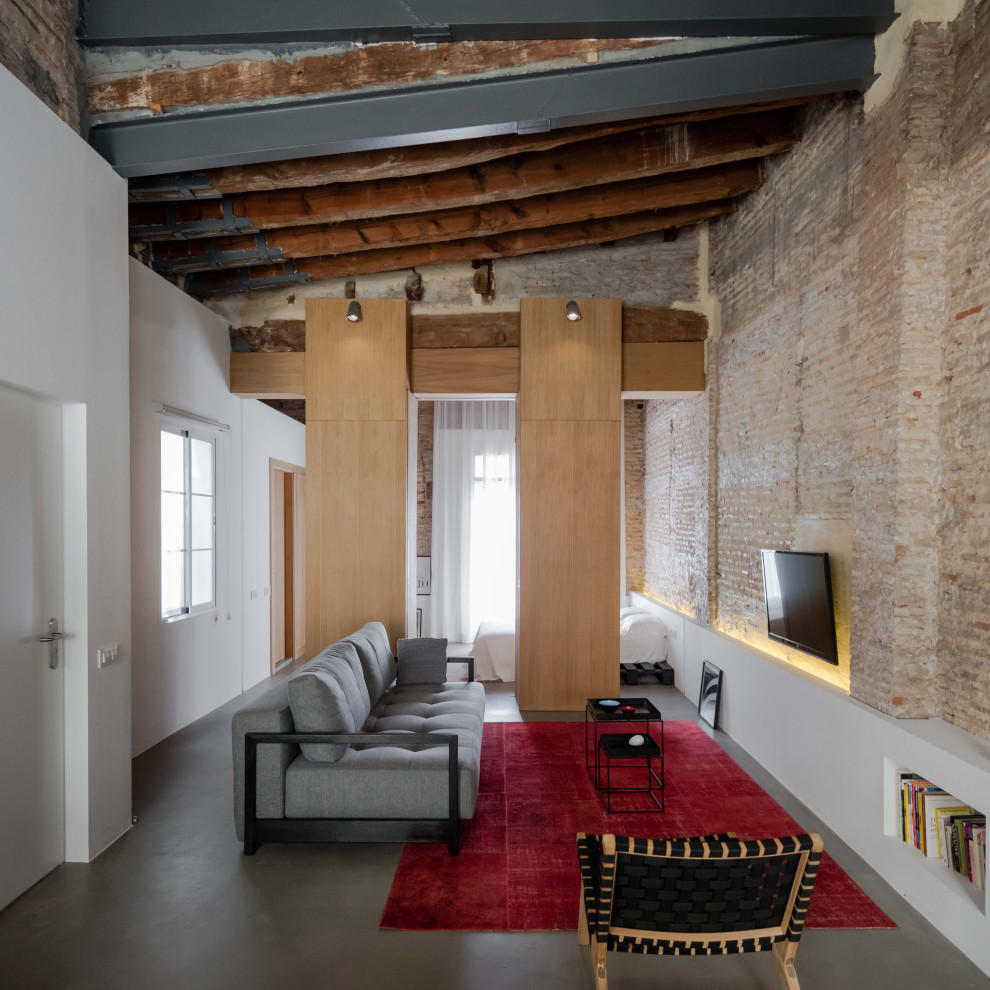 Immagine di un soggiorno industriale aperto e di medie dimensioni con nessun camino, TV a parete, pavimento grigio, pareti bianche e pareti in mattoni