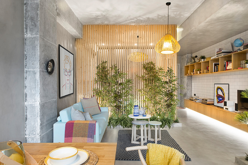 Стильный дизайн: открытая гостиная комната в современном стиле с серыми стенами, бетонным полом, отдельно стоящим телевизором, серым полом и синим диваном - последний тренд
