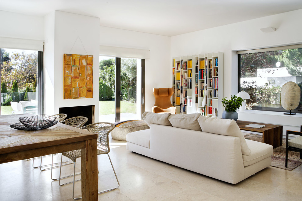 Cette image montre un grand salon design avec un mur blanc, un sol en calcaire et un manteau de cheminée en plâtre.
