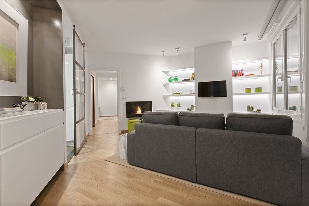 This is an example of a small modern open concept living room in Bilbao with a library, white walls, light hardwood floors, a ribbon fireplace, a metal fireplace surround, a wall-mounted tv and yellow floor.